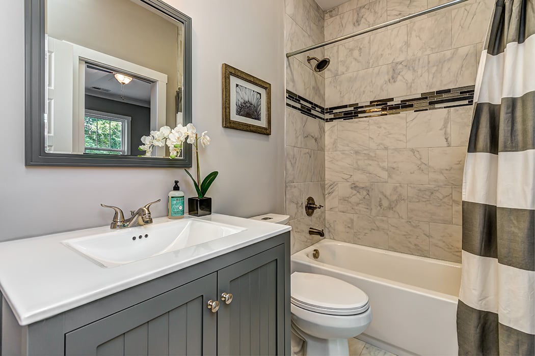Bathroom with gray cabinet white countertop with gray framed mirror shower with white and gray tile white bathtub