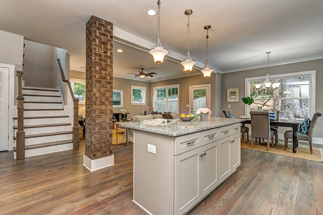 Kitchen open to living room and dining room gray walls wood floors white cabinets gray countertops brick column