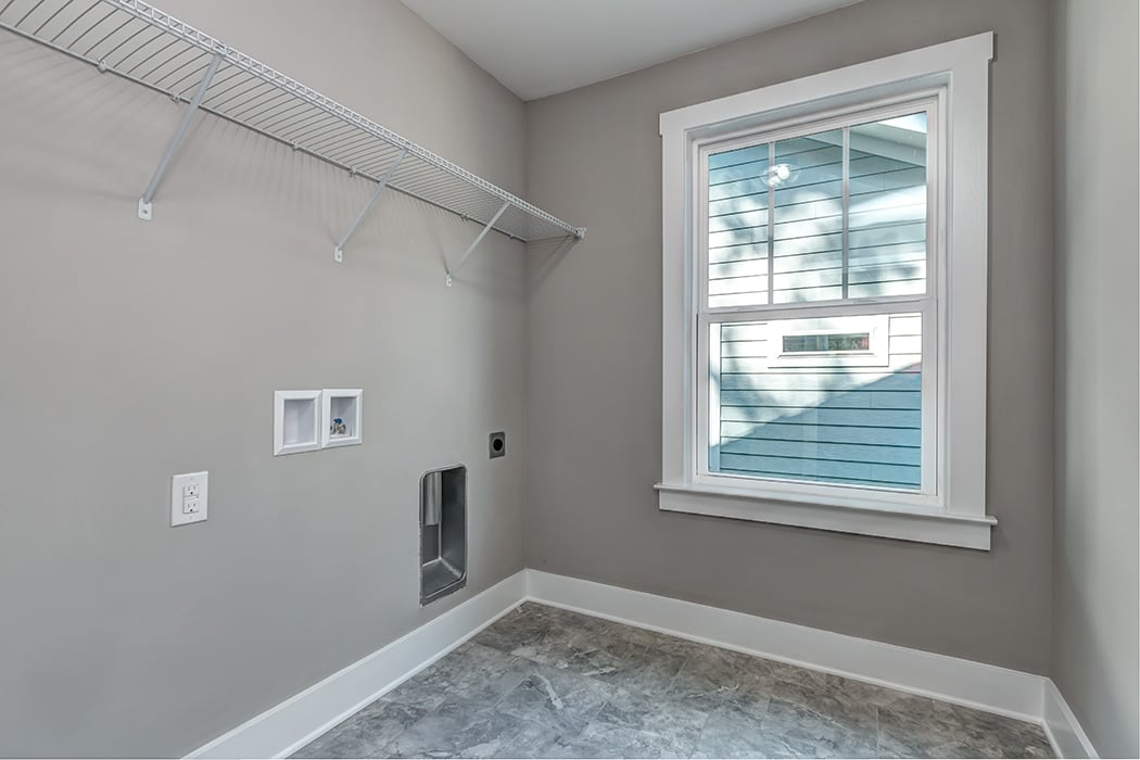 Empty laundry room with gray walls tile floor white baseboards window with white trim washer dryer hookups wire rack shelf