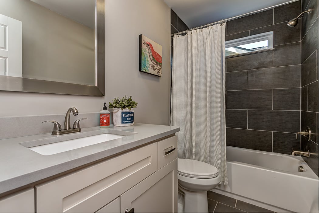 Bathroom with white cabinets light gray countertops nickel frame mirror gray tile floors gray tile shower white bathtub