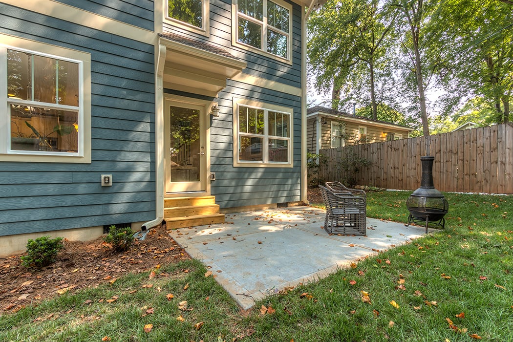 Blue siding two story home with light brown details and back patio with two chairs and fire pit fenced in yard