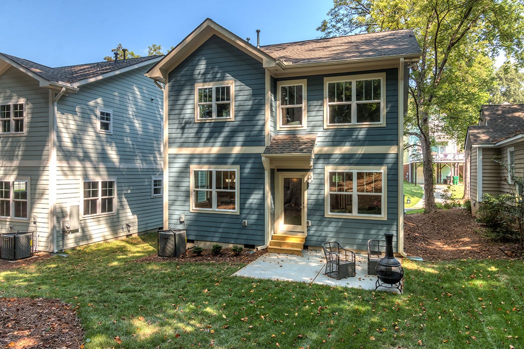 Blue siding two story hime with cream colored details and front porch with two chairs and fire pit
