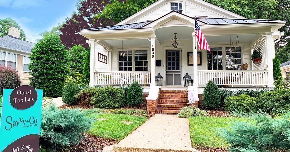 White siding home with large front porch with brick steps white columns and railings with blue and brown Savvy sign in front yard