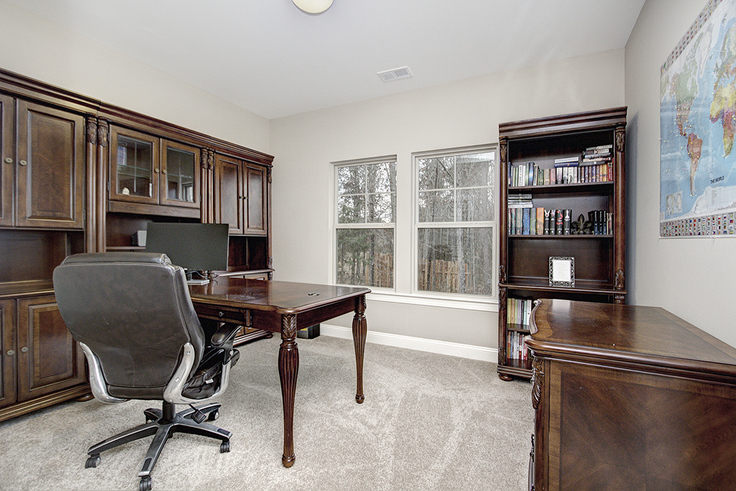 Home office with neutral color walls light carpet double windows dark wood furniture