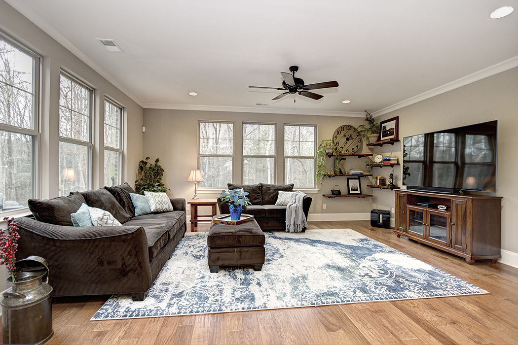 Living room with gray walls white trim dary ceiling fan light wood floors windows on two walls