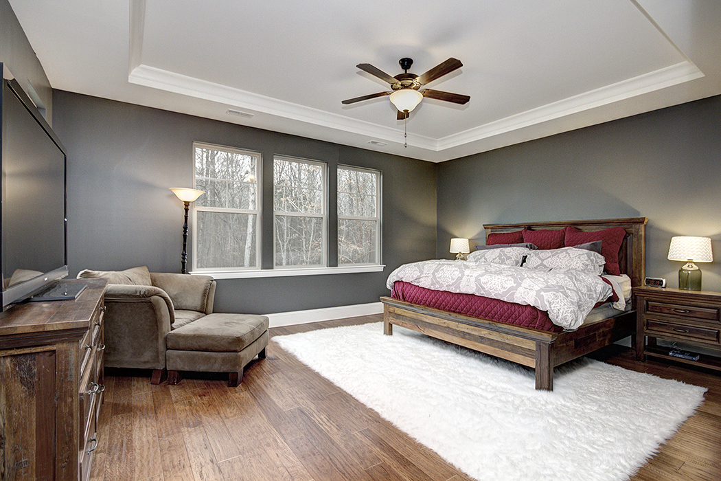 Bedroom with dark gray walls tray ceiling dark wood ceiling fan wood floors white baseboards three windows