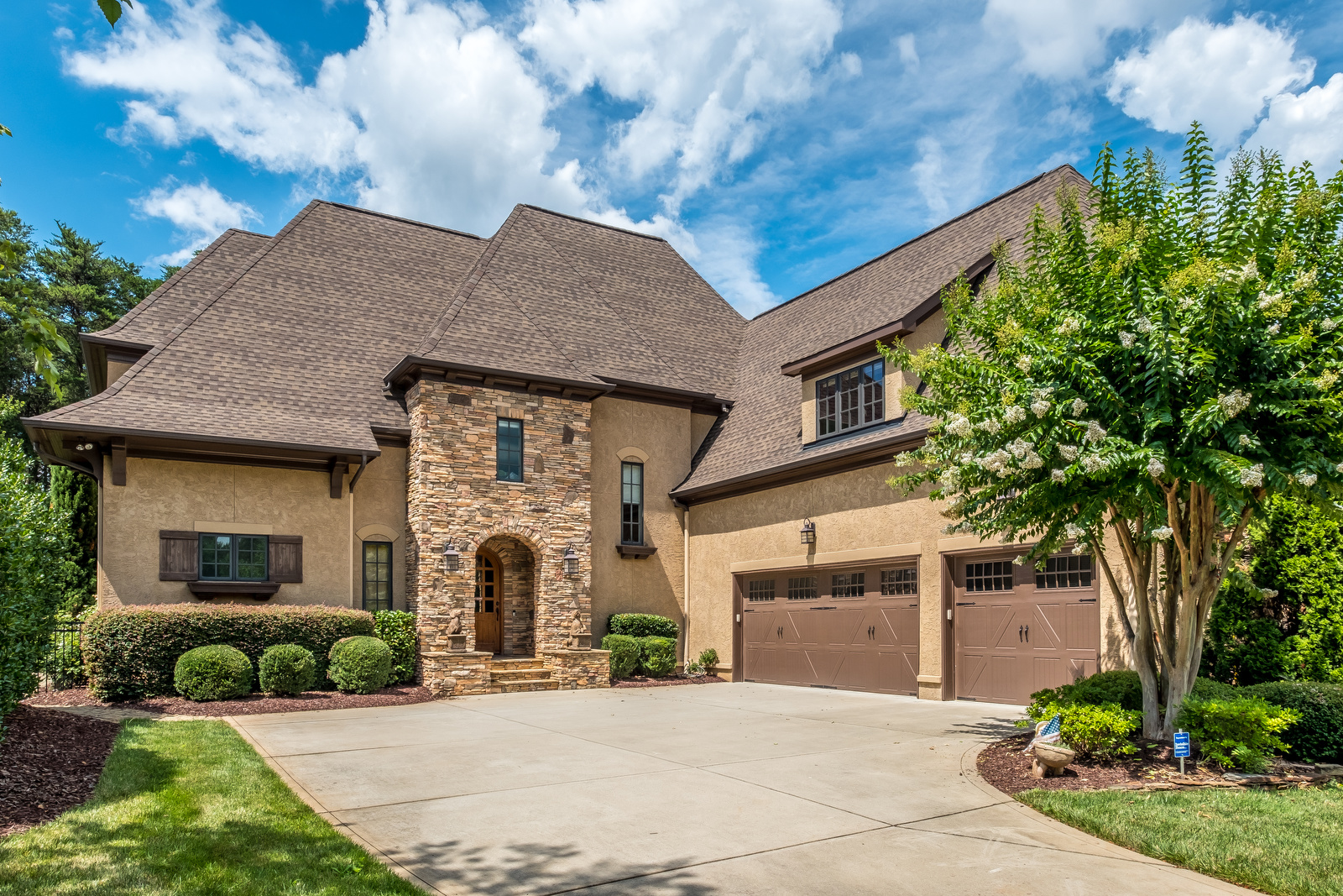 Large two story brown stone and stucco home with brown two car garage green front yard with manicured landscaping