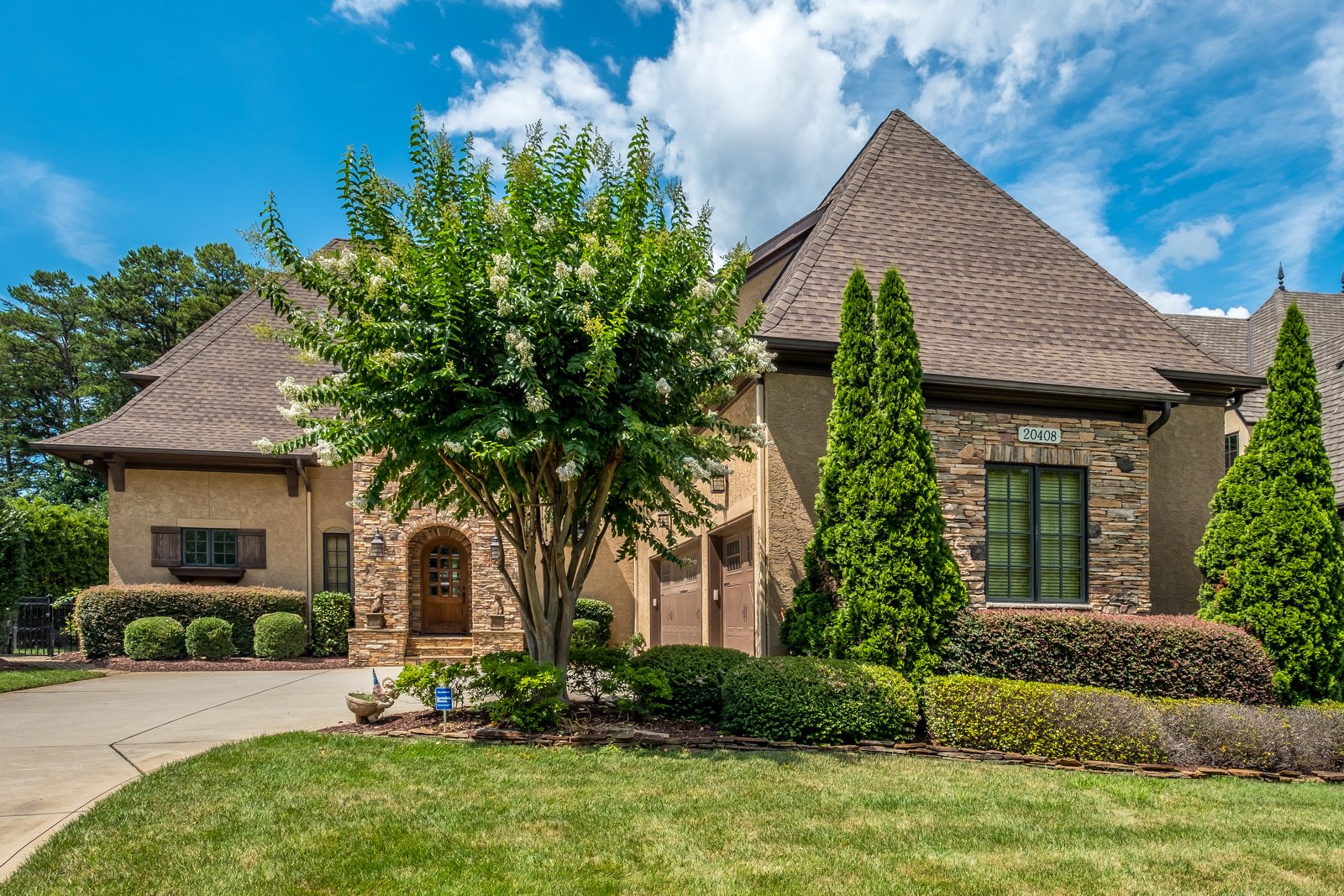 Large two story brown stone and stucco home with brown two car garage green front yard with manicured landscaping