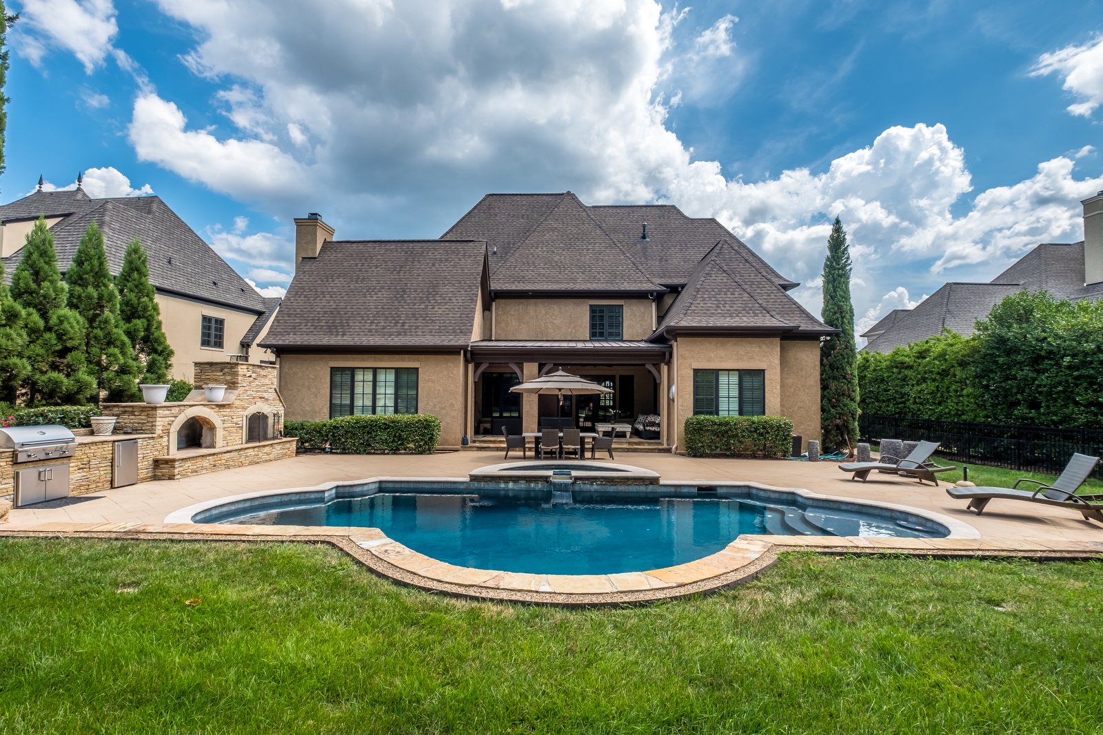 Backyard with pool with stone details eating area hot tub and built in fireplace and grill area with playground in background