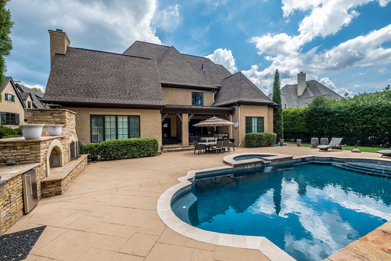 Large two story home backyard with beautiful blue pool eating area built in grill area and manicured trees