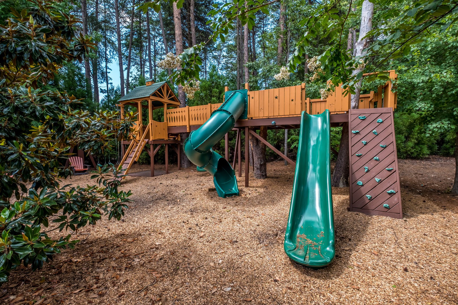 Backyard with kids playground with green slides and green details surrounded by trees