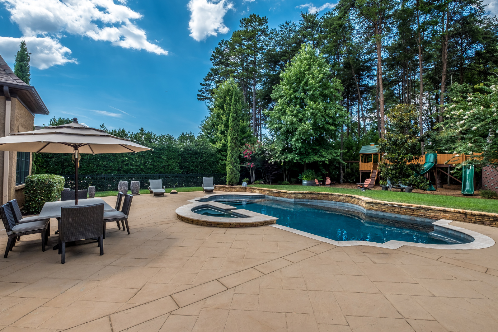 Backyard with built in pool playground in background eating area and manicured trees