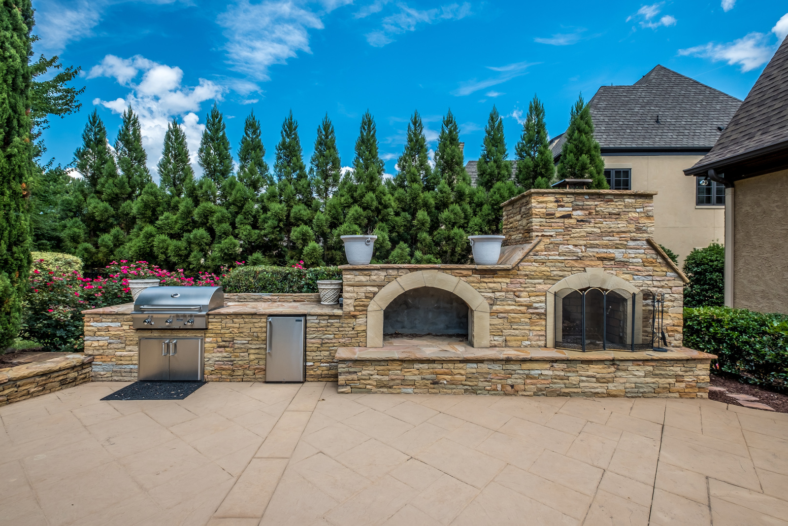 Backyard with built in grill area drink fridge pizza oven and fireplace stone details manicured trees in background