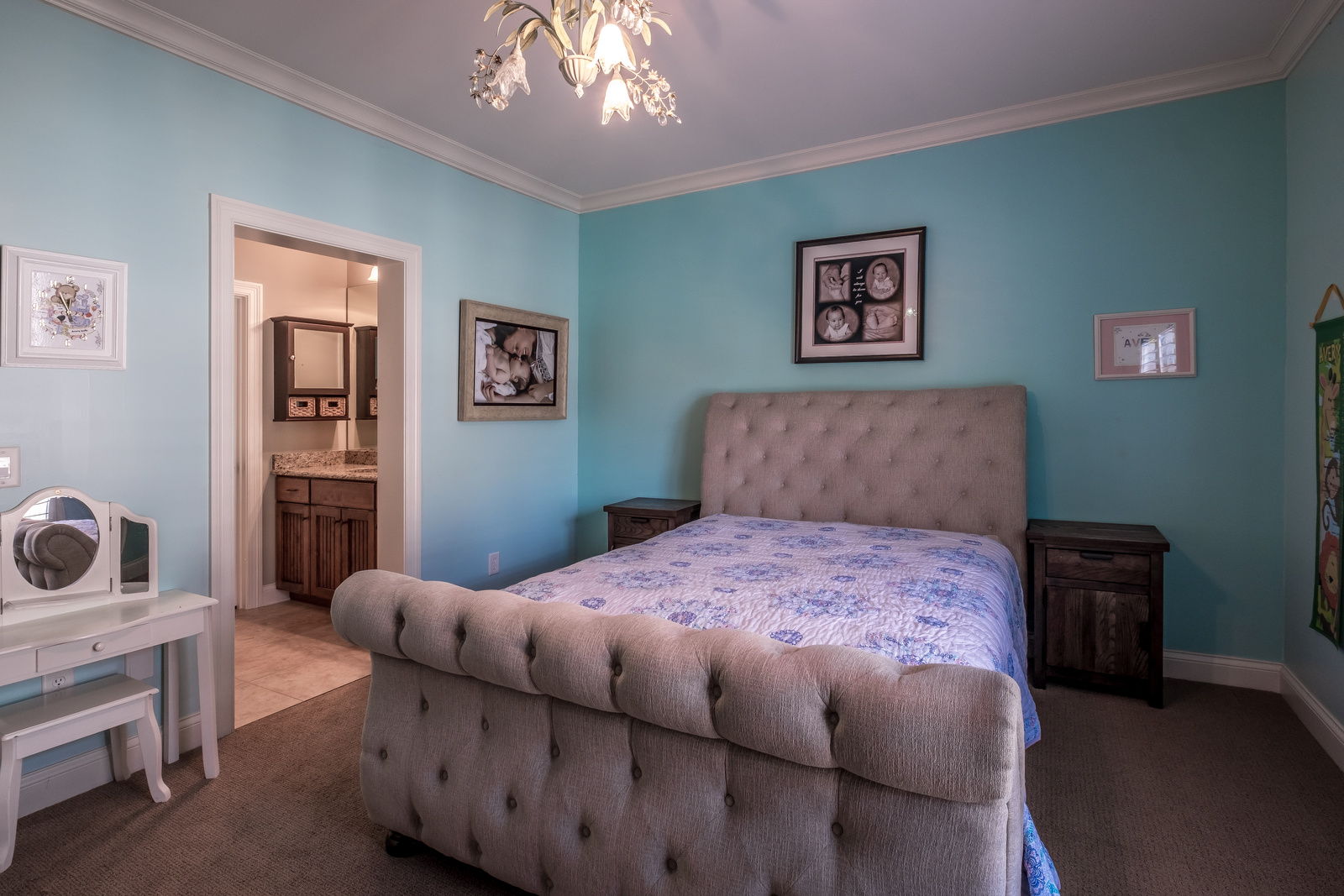 Bedroom with light blue walls carpet flooring white trim and chandelier open to bathroom