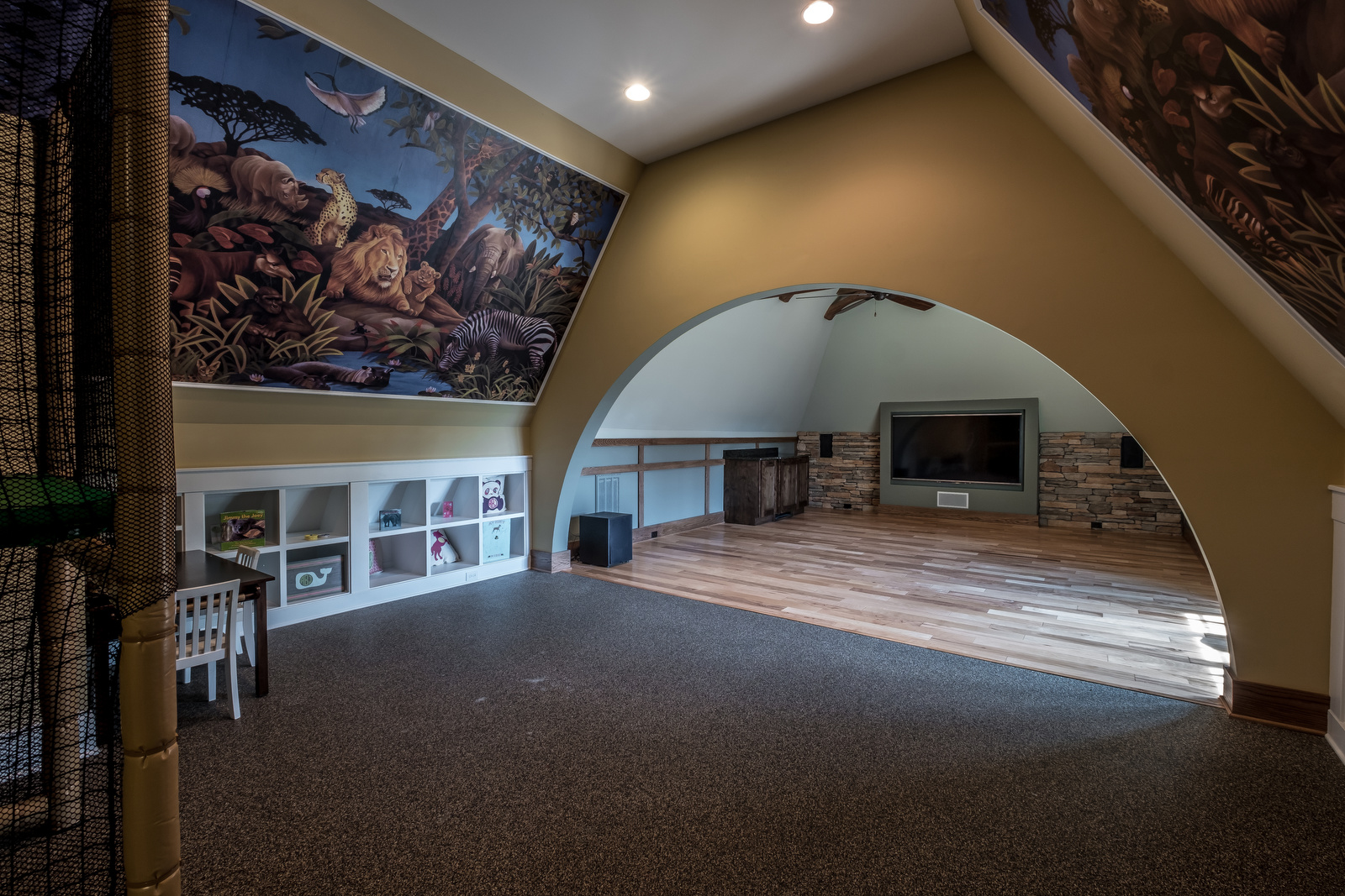 Large playroom with arch dividing the room light brown walls recessed lighting two huge animal murals on the walls