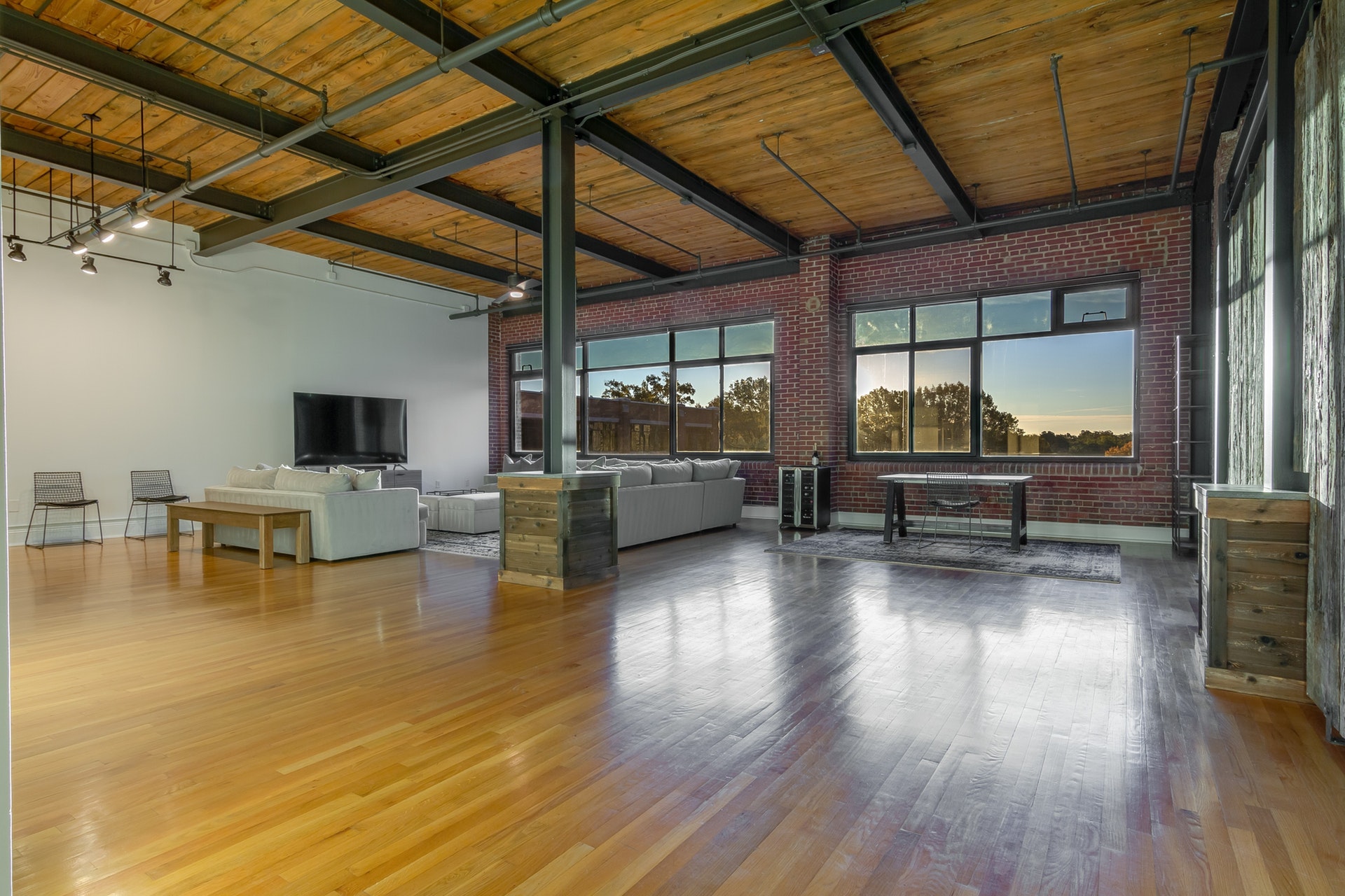 Living room with office area high wood ceilings exposed pipe black beams white wall red brick wall large black trim windows