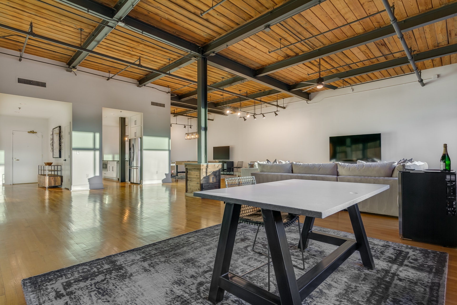 Dining room open to kitchen living room and entryway light wood floors white walls wood ceilings exposed pipes black beams ceiling fan