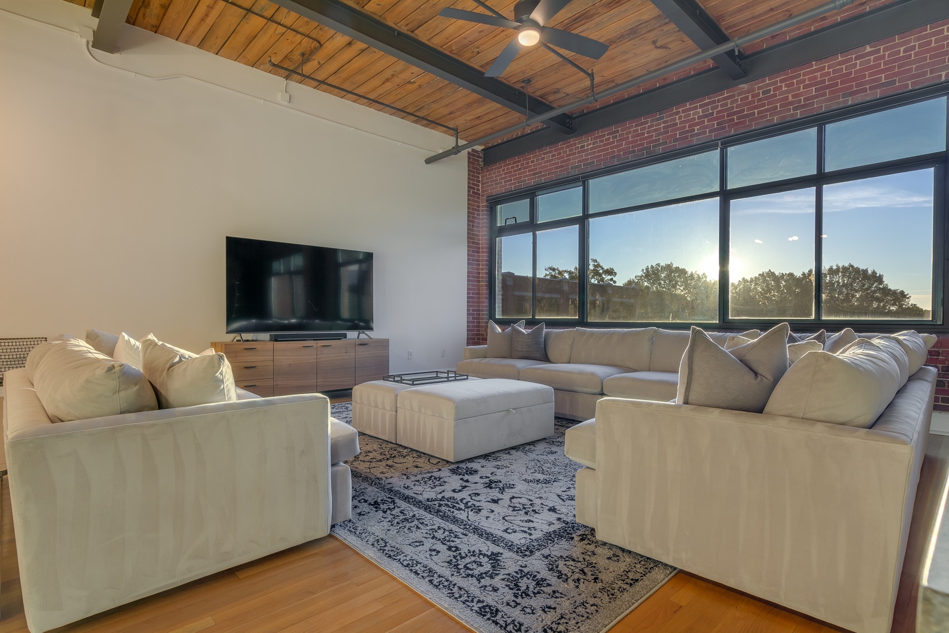 Living room with white wall and red brick wall with black framed windows light wood floors light wood ceiling
