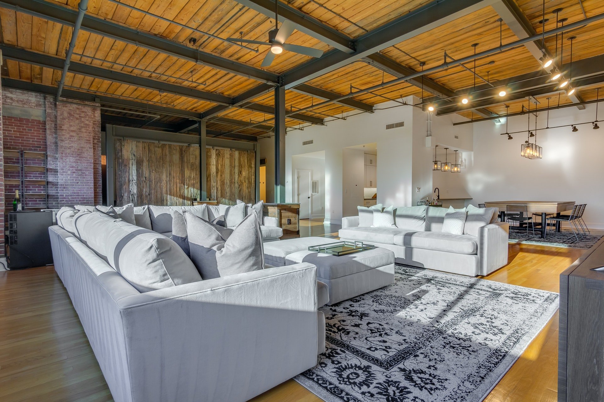 Living room open to kitchen and dining room industrial style white and brick walls light wood floors light wood ceilings exposed pipes