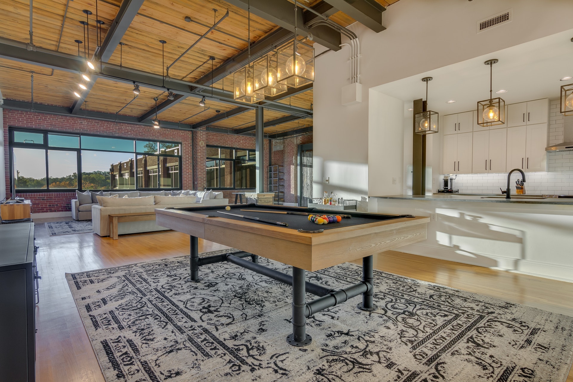 Open living room kitchen and game room wood ceiling exposed pipes track and pendant lighting brick walls and white walls