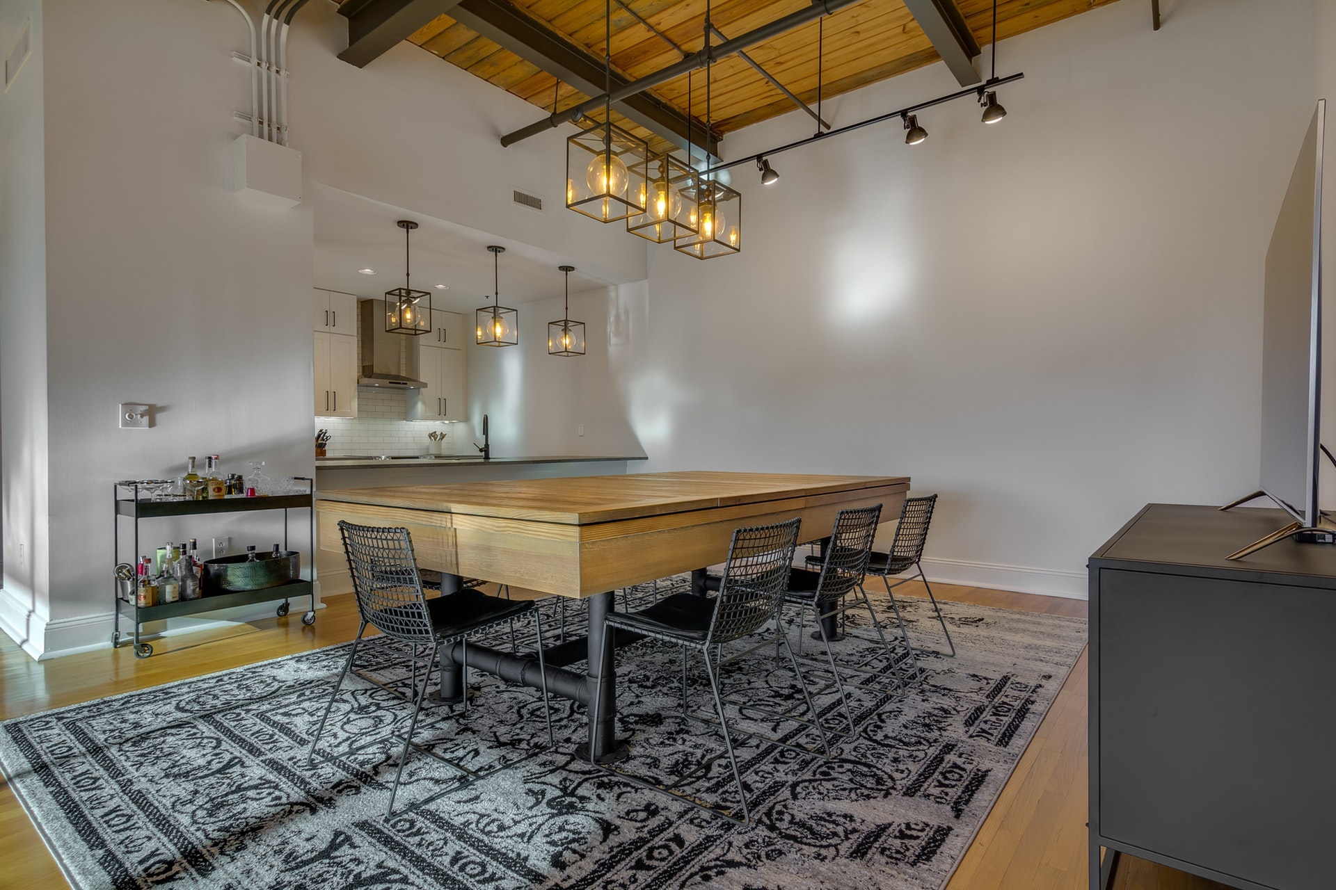 Dining room with white walls wood ceiling with exposed piping light wood floors track lighting pendant lighting over dining table