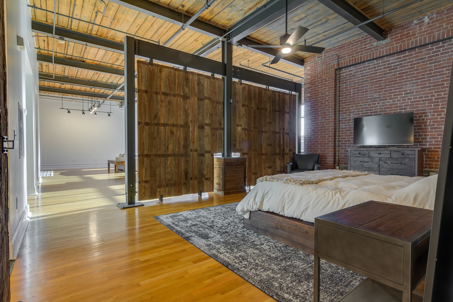 Bedroom with red brick wall light wood floors wood ceilings with exposed pipes wooden partition