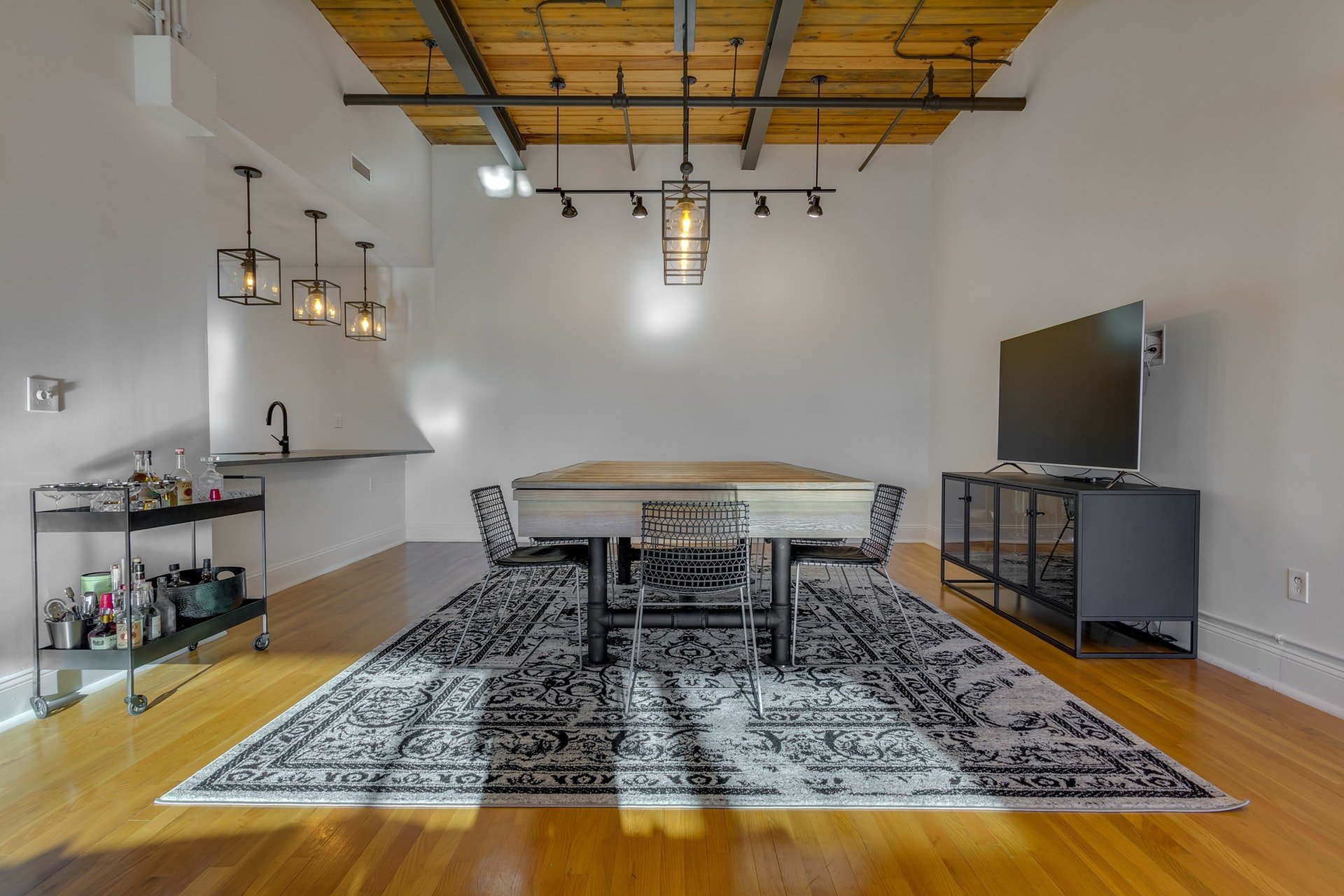 Dining room with white walls wood ceiling with exposed piping light wood floors track lighting pendant lighting over dining table