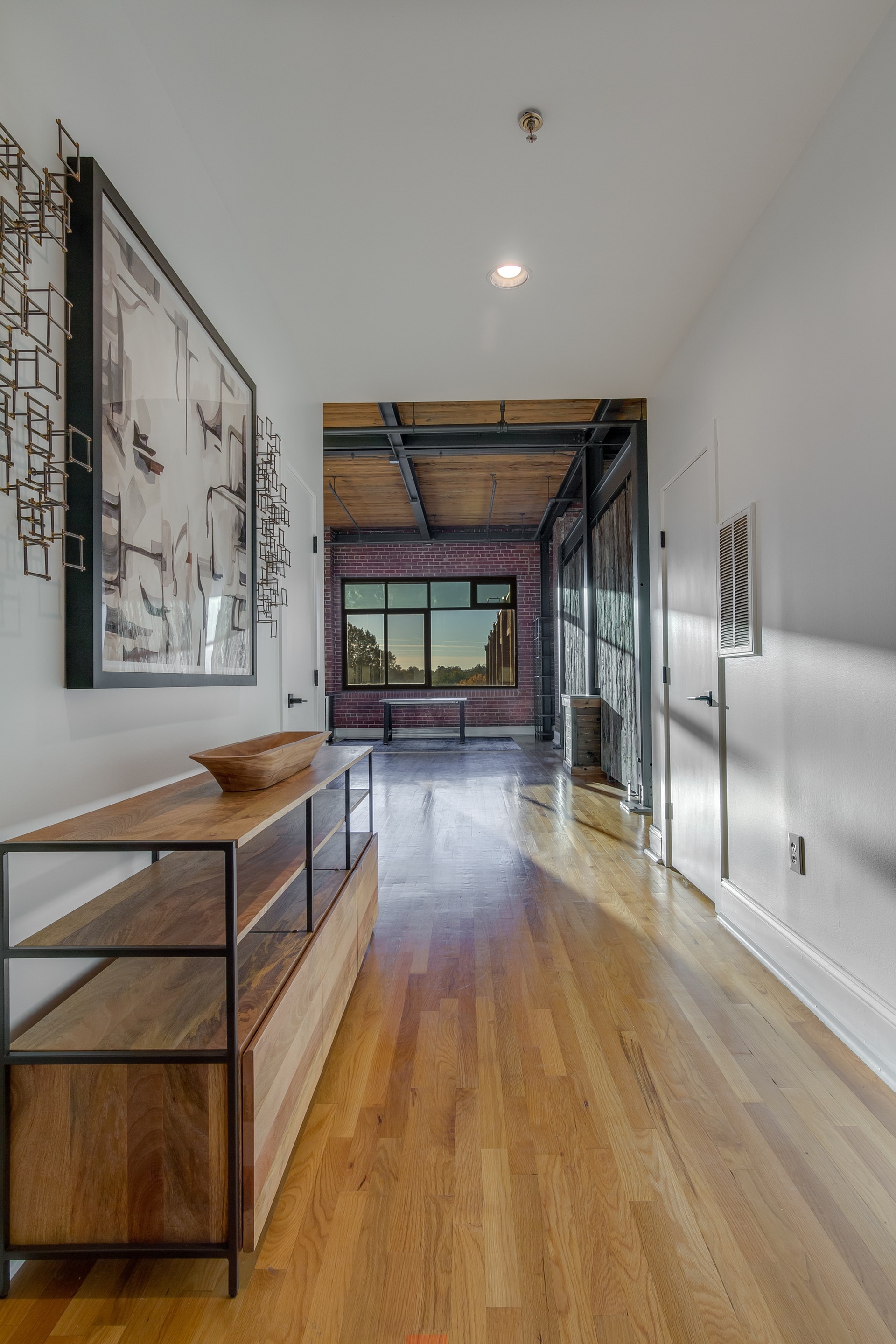 Large entry way light wood floors white walls white doors leading to brick wall large black framed window