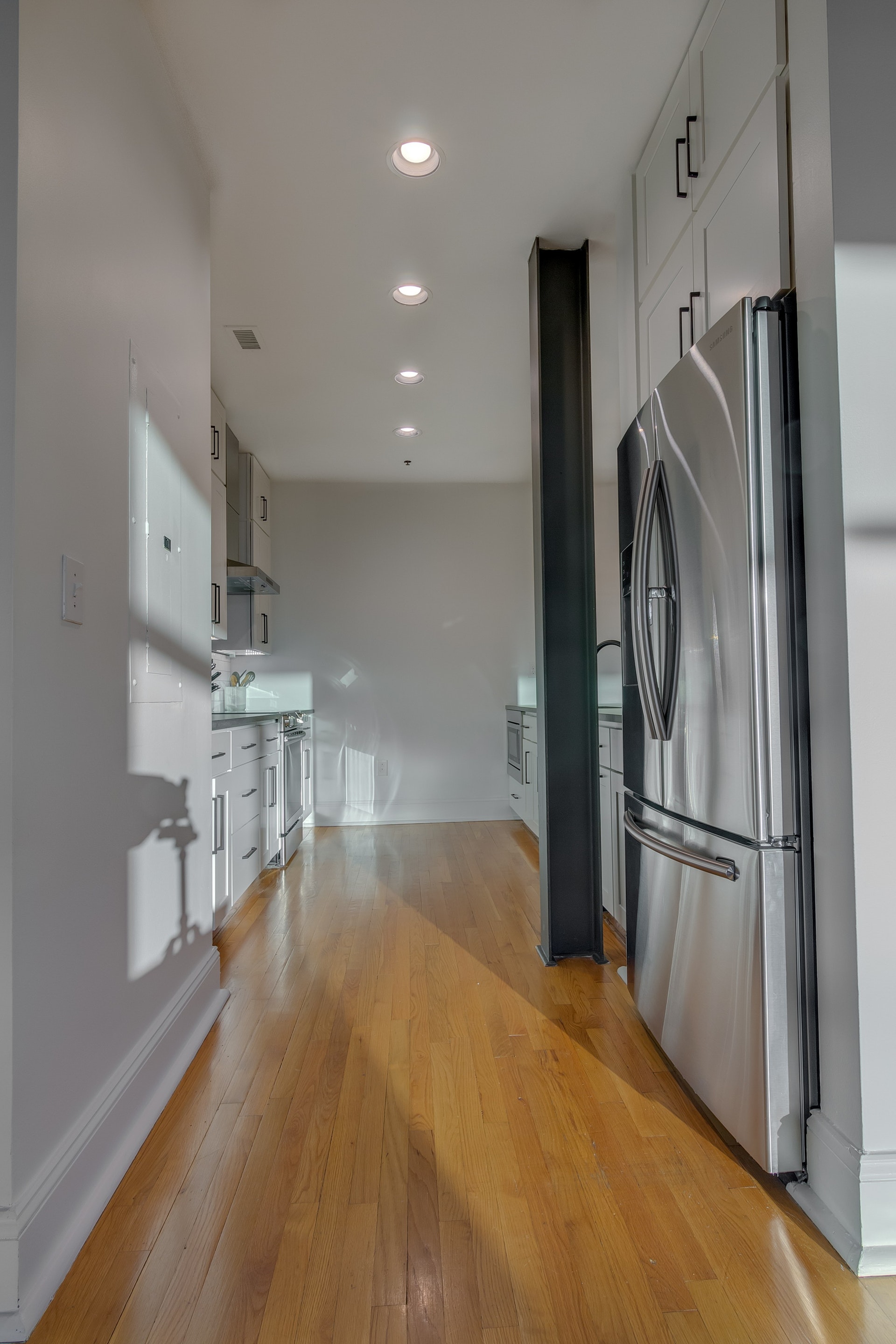 Galley style kitchen with light wood floors white walls black steel beam in the middle white cabinets stainless steel appliances