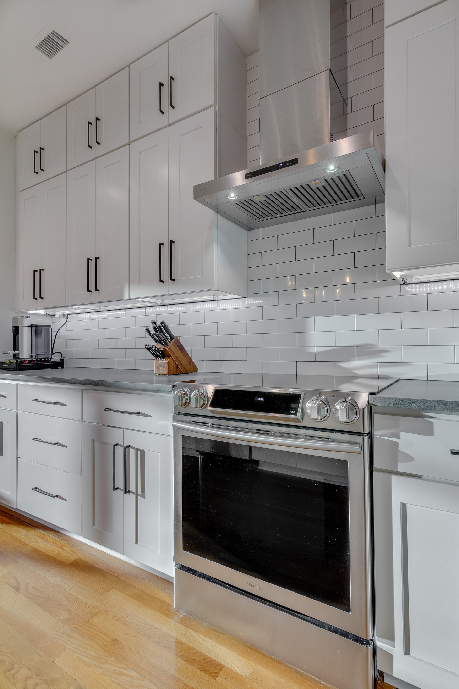 Kitchen with light wood floors white cabinets new appliances white subway tile backsplash