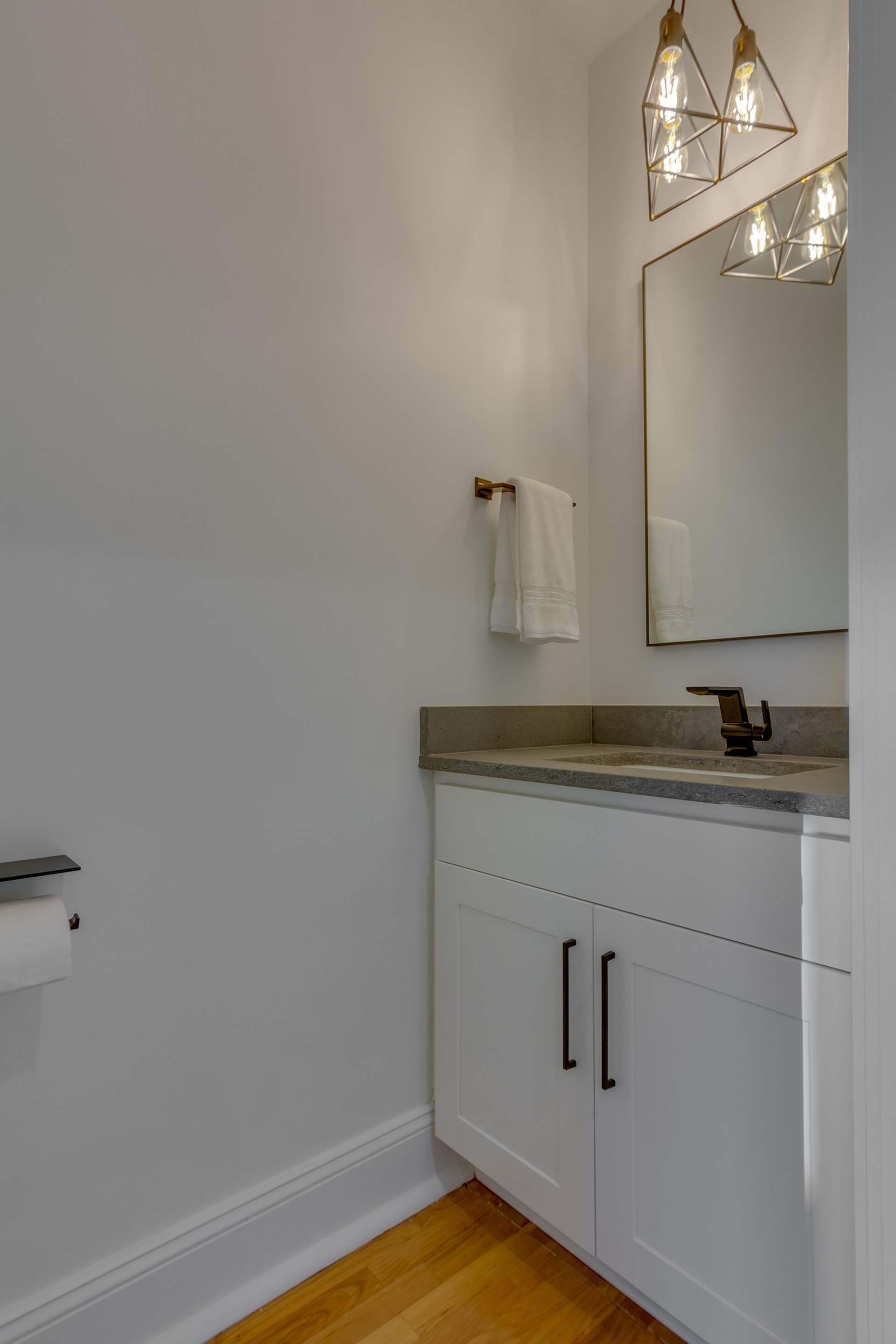 Bathroom with white walls light wood floors white cabinets gray countertops bronze framed mirror