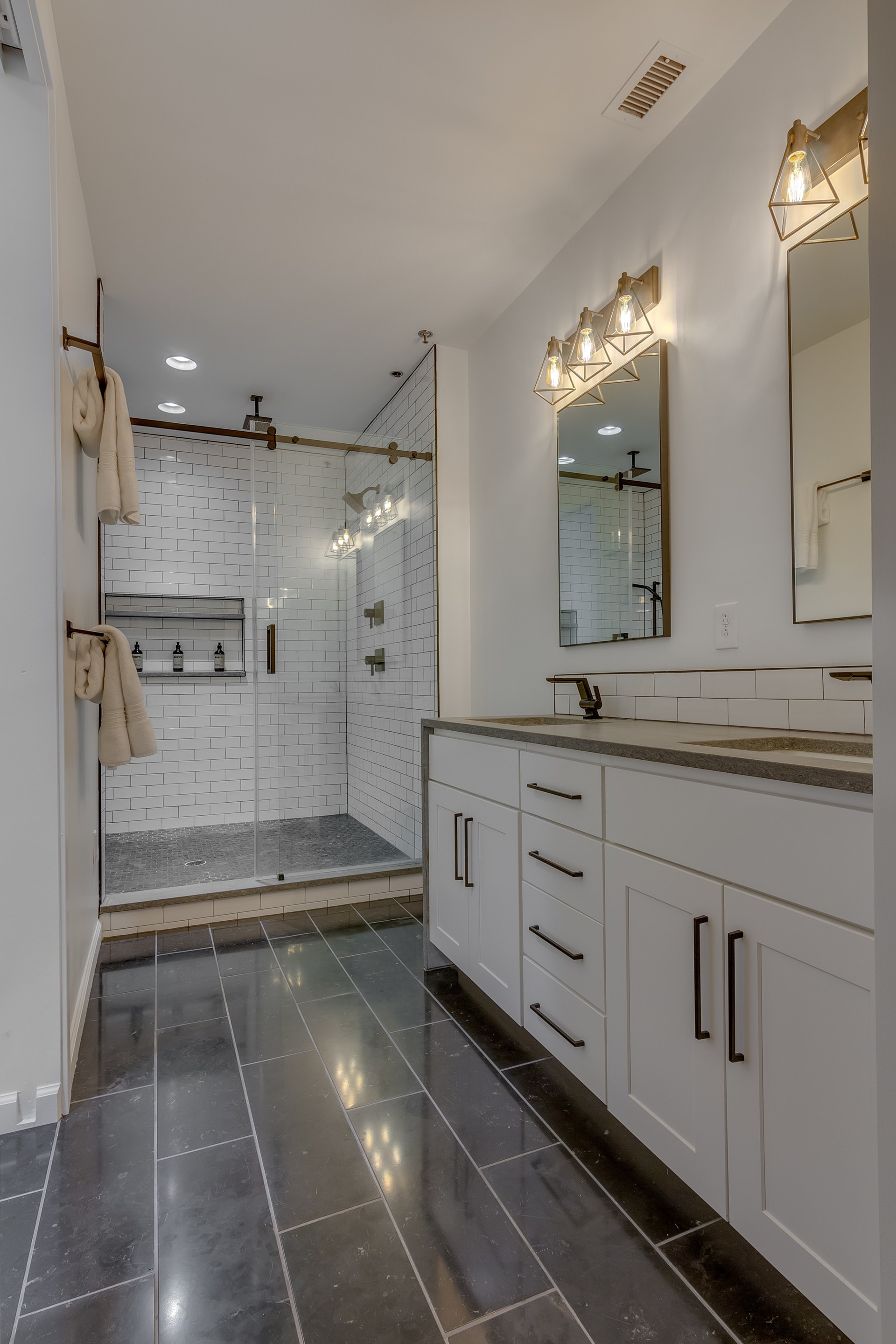 Bathroom with gray tile floors white walls white cabinets gray countertop oil rubbed bronze hardware white tile walk in shower