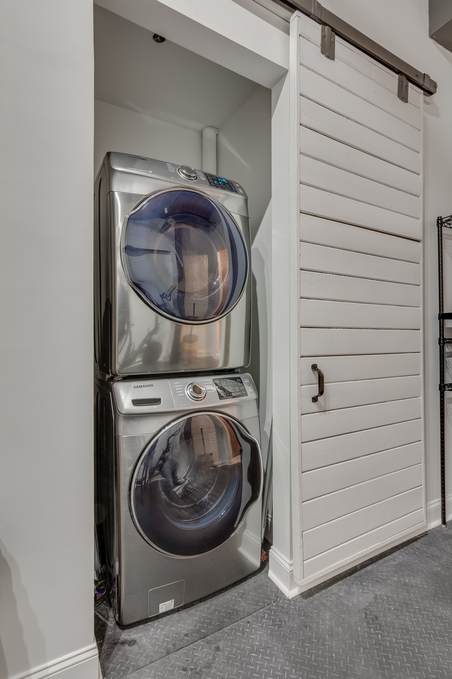 Stainless steel front loading stacked washer and dryer with white sliding barn door in front