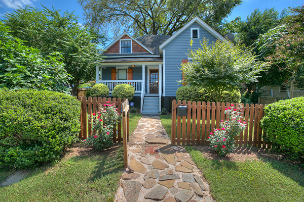 Blue siding home with brown shingles brown shutters wood front door wooden fence around yard stone pathway