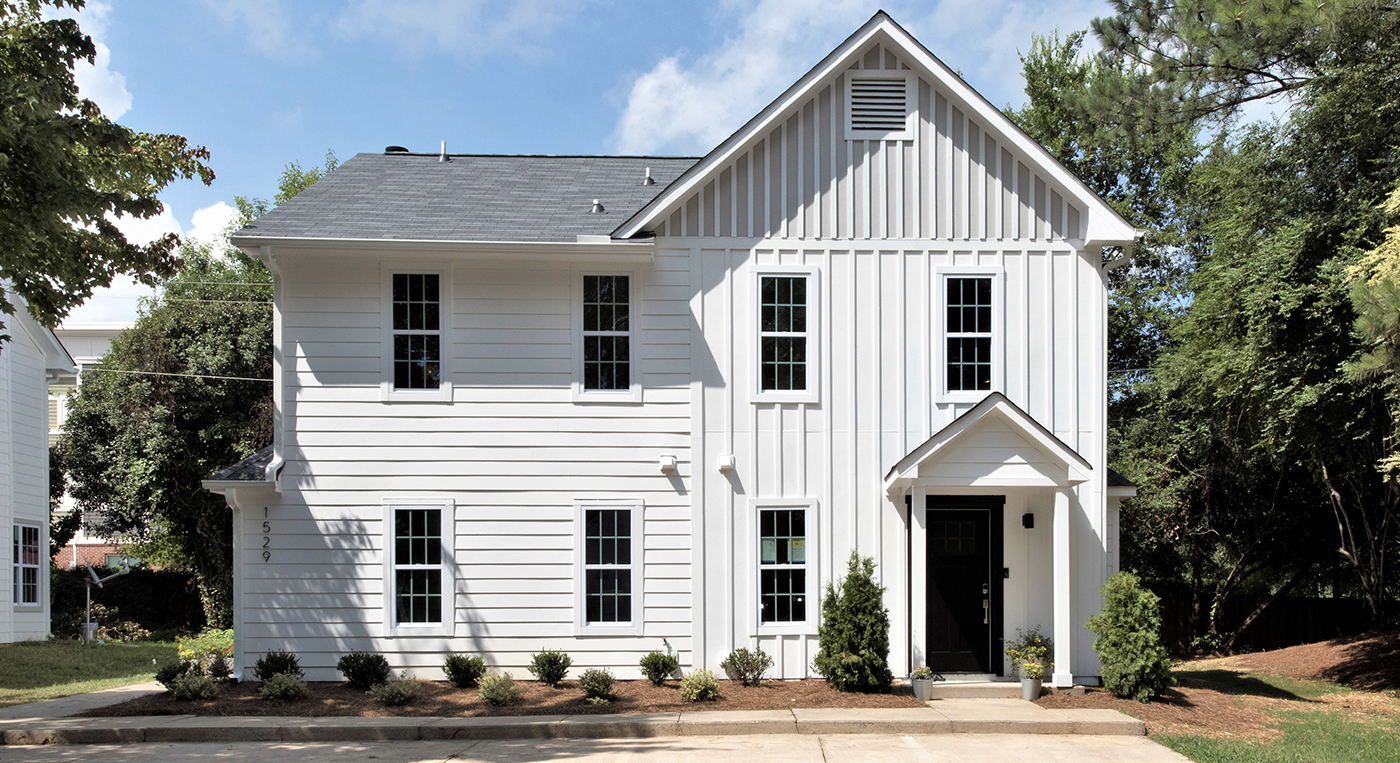 White two story condo building with horizontal and vertical siding black front door siding around building with trees around it