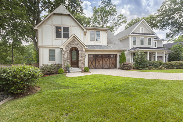 White and tan home with stone arch around front door brown barn door style two car garage brick driveway green grass front yard fenced in backyard