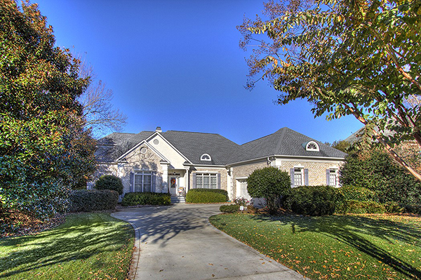 Light gray brick home with light blue shutters bushes around perimeter two car garage with circular cement driveway