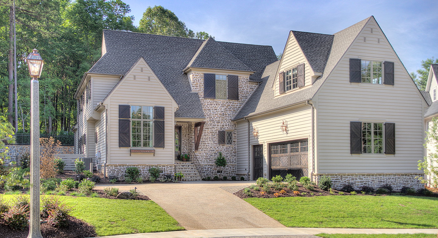 Large two story home mix of tan siding and light brick with black shutters two car garage landscaped with flowers and bushes