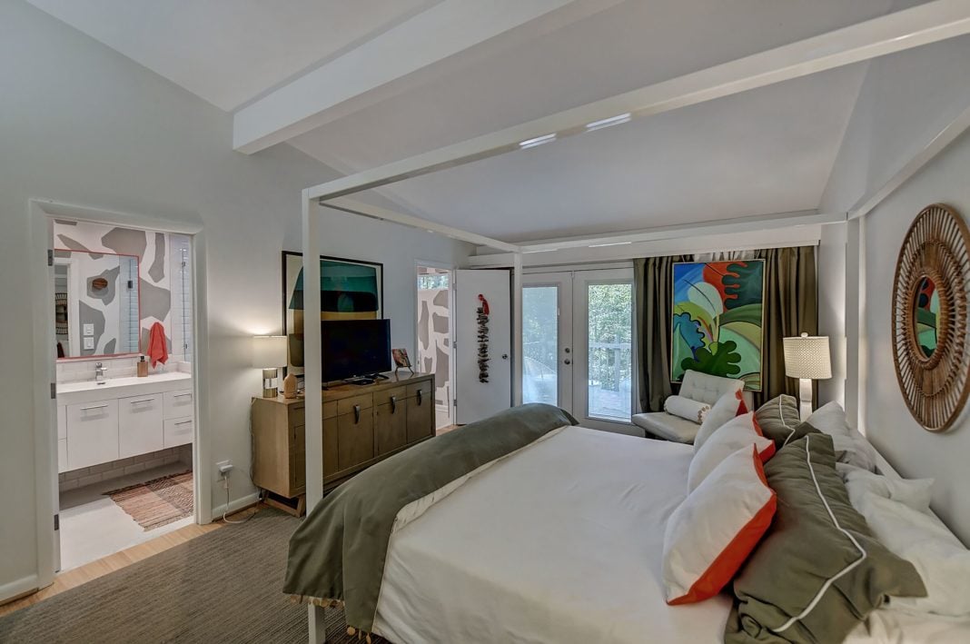Master bedroom with glass doors to backyard white walls light wood floors open to master bathroom