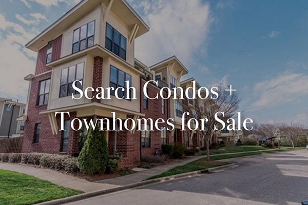 Red brick three story condo building with black trim windows grass surrounding it with sidewalk and street in front