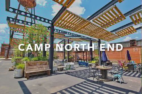 Patio with cement floors and wooden pallets as the seating tables and chairs and sitting area with the words Camp North End typed over the image