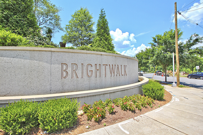 Concrete sign with Brightwalk engraved in it flowers planted in front and tree lined sidewalk