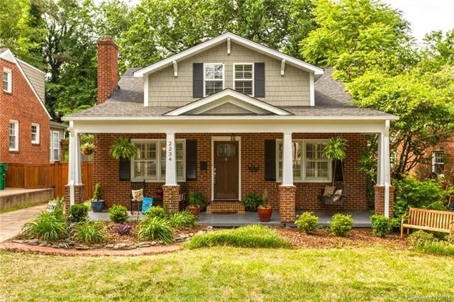 Red brick home with gray shingles and front porch with rocking chairs and porch swing