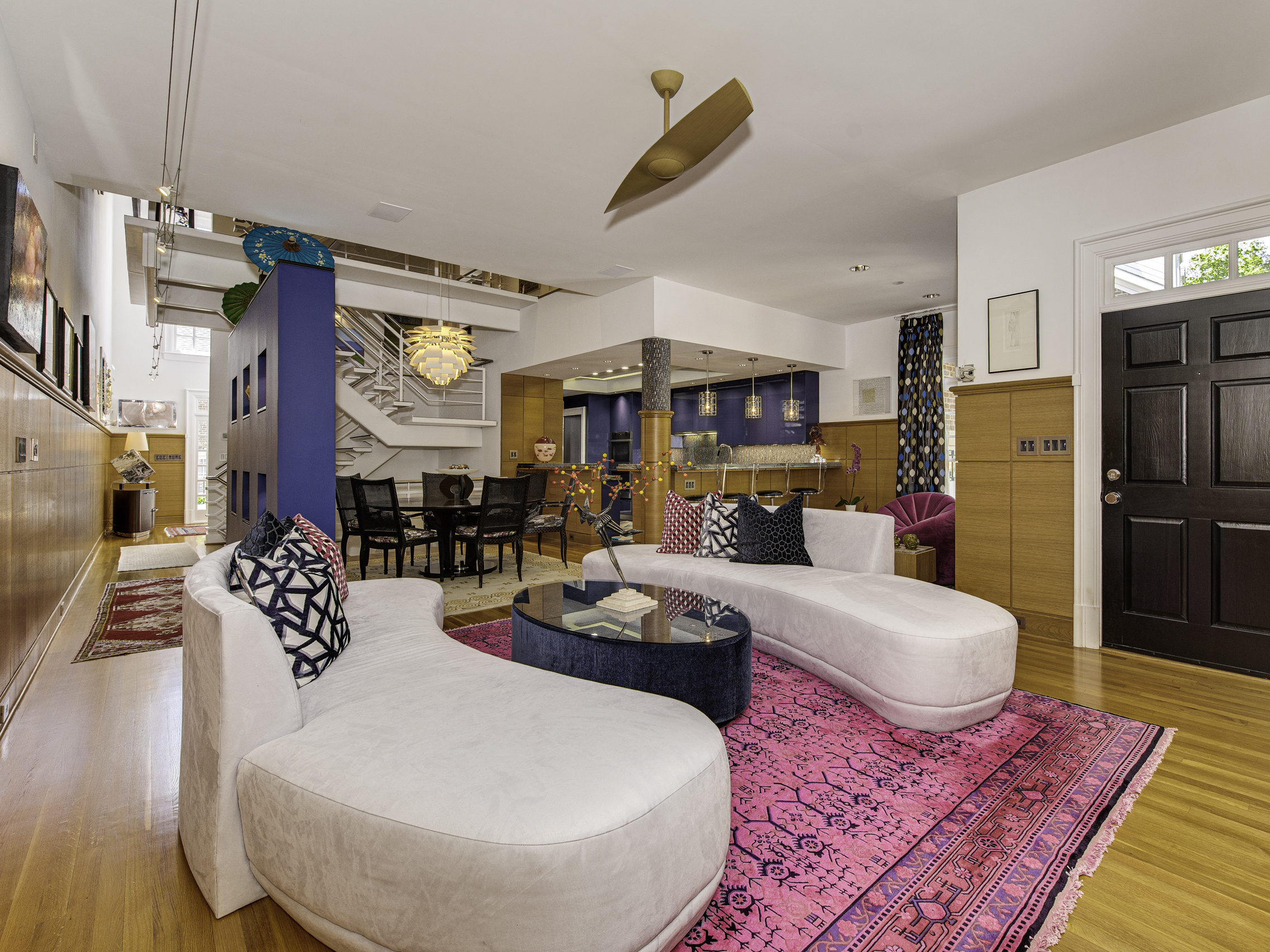 Living room open to dining room and kitchen with wood floors wood paneling on walls and white walls with black front door
