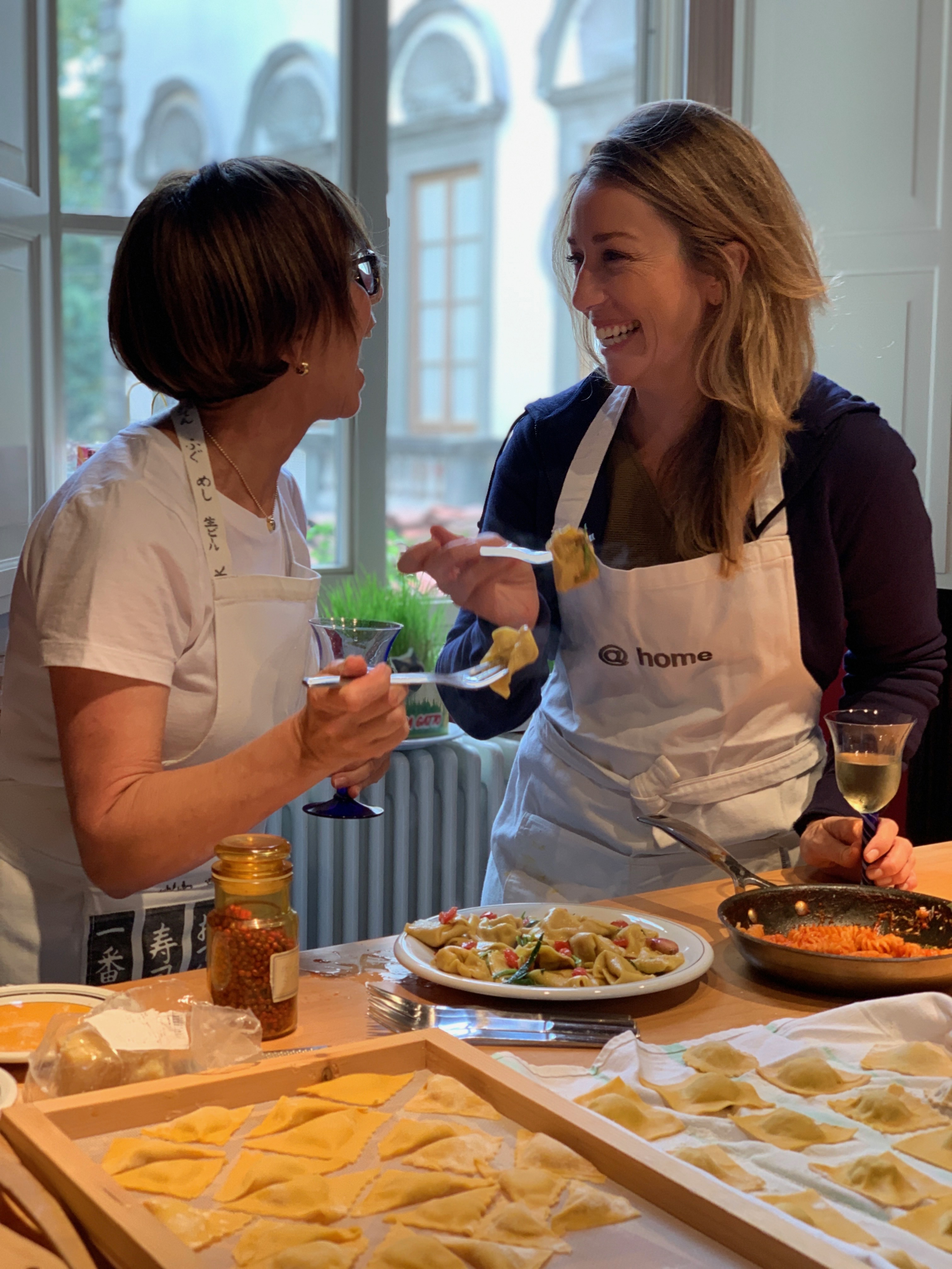 Sarah Martin and Client in Italy_2 Sarah Martin wearing a white apron standing with a lady wearing a white apron with homemade pasta around them both holding forks with pasta on them