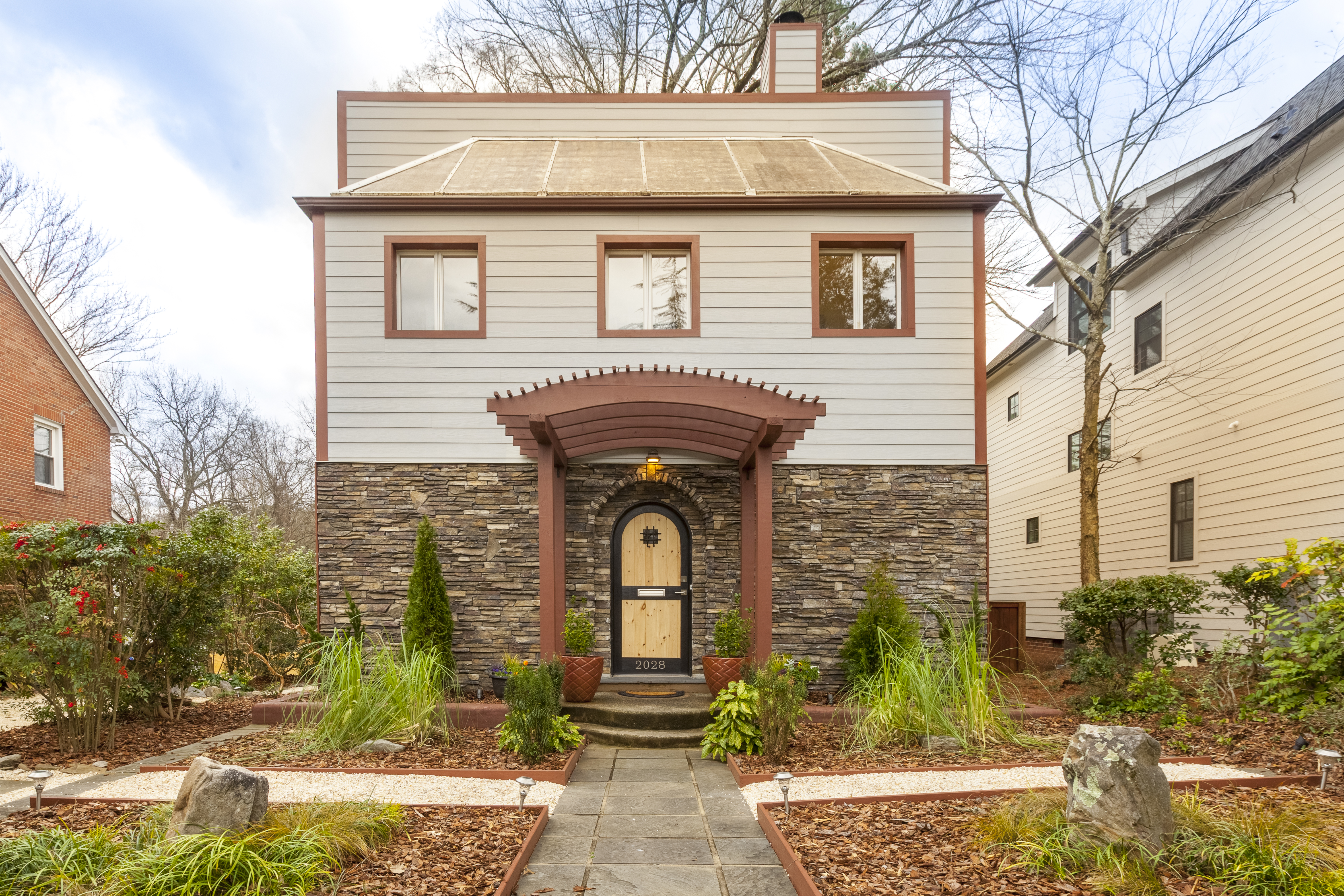 Two story modern home with stone on first floor and white siding on second floor with brown trim around home and windows