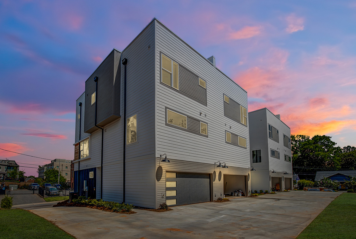 Three story townhomes with two car garages and blue and gray siding with white framed windows and cement wraparound driveway