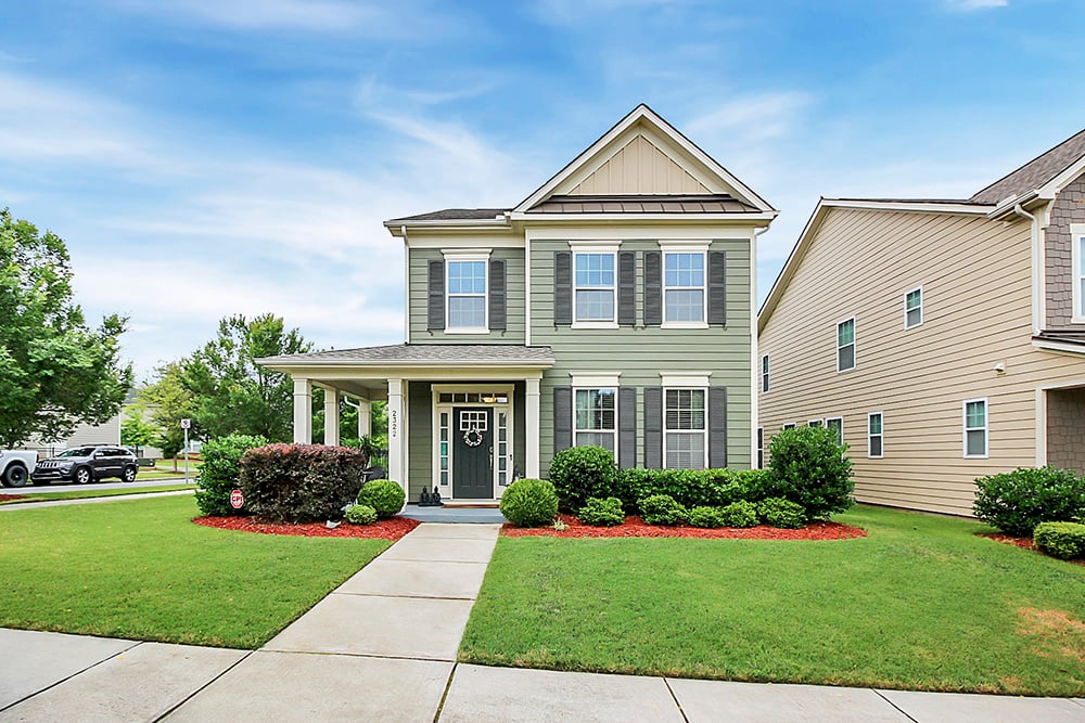 Two story home with green siding and green shutters and green front door with front porch that wraps around the side of the home