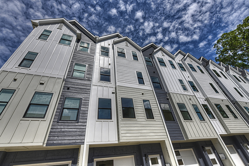 Row of four story townhomes with mix of white gray and cream horizontal and vertical siding with one car garages and white doors