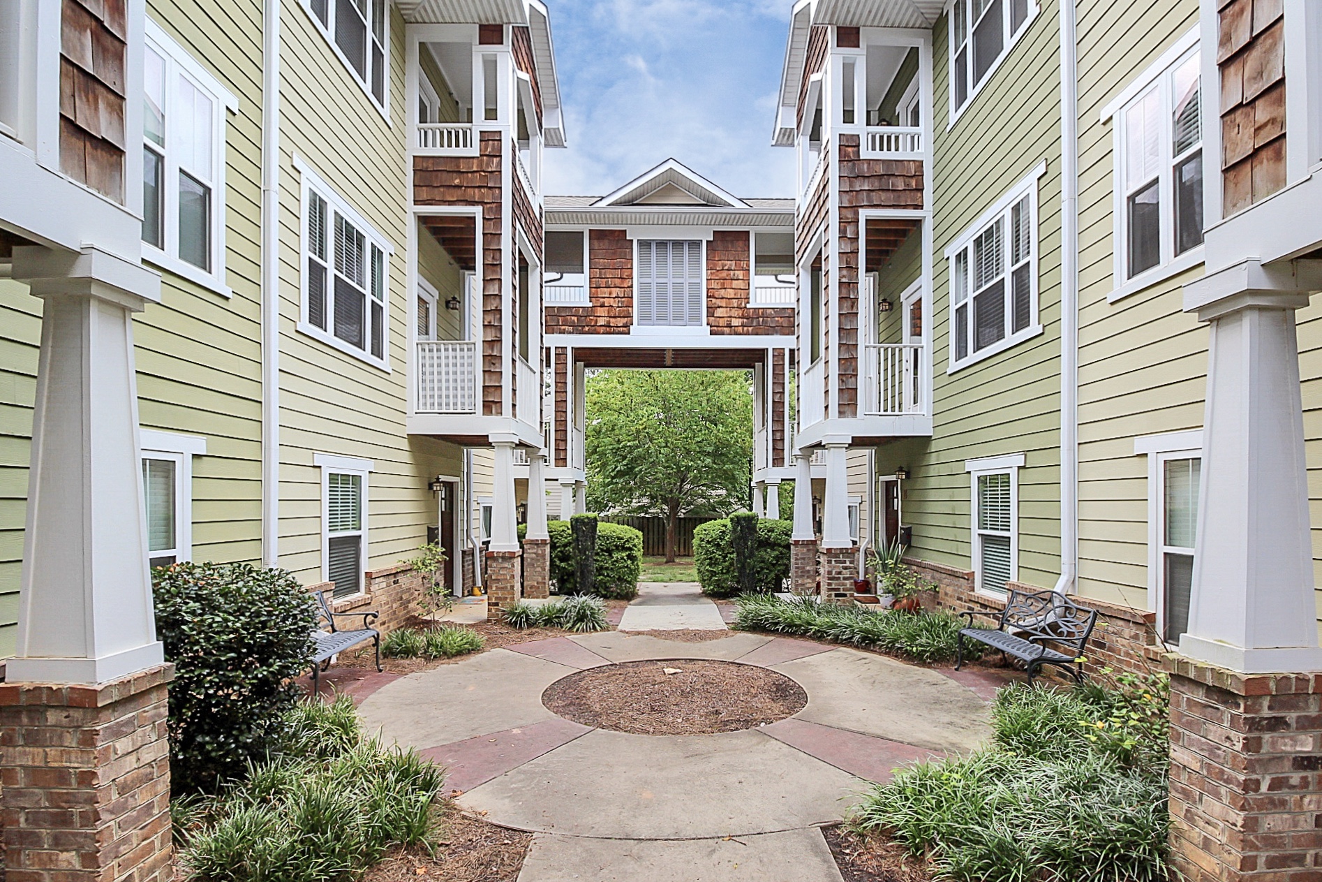 Condo building courtyard with light green siding and brown brick with brown shingles and white framed windows and patios with white railings and columns